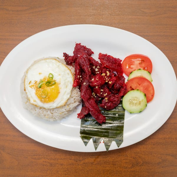 Filipino Tapsilog with bright red cured beef, fried egg, garlic rice, and sliced vegetables.