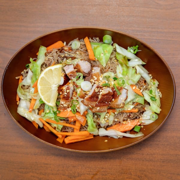 Filipino Pancit Palabok with crispy pork belly, cabbage, carrots, and a lemon wedge in a brown bowl.