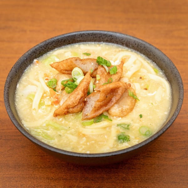A black bowl of creamy Filipino pancit molo soup with noodles, fried pork, and green onions.