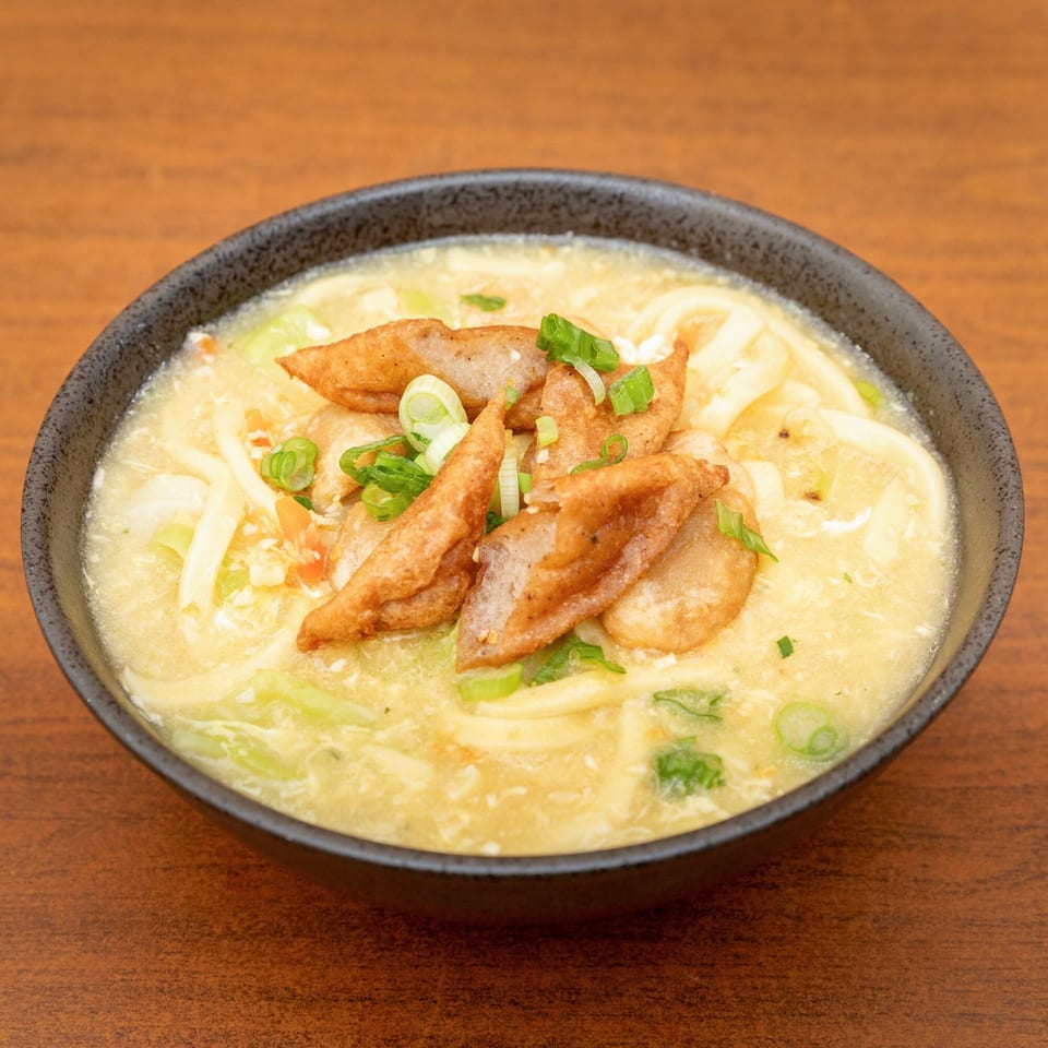 A black bowl of creamy Filipino pancit molo soup with noodles, fried pork, and green onions.