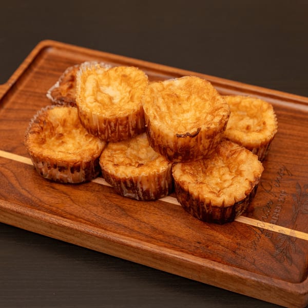 Golden-brown Tindahan Pinoy Filipino cassava cakes in paper liners on a wooden serving tray.
