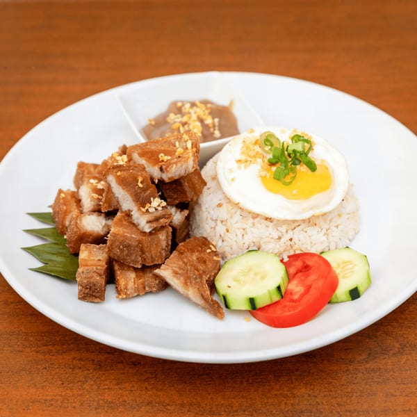 Filipino crispy pork belly (Lechon Kawali) with garlic rice, fried egg, and vegetables on a white plate.