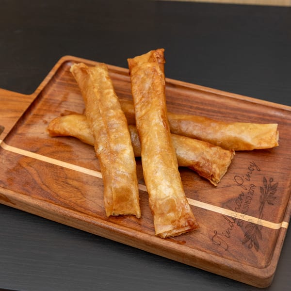Four golden-brown Filipino lumpia rolls, or fried spring rolls, on a wooden serving board.