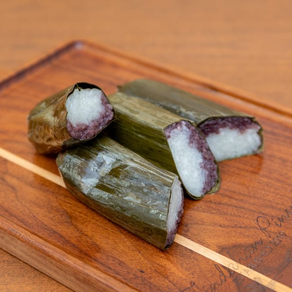 Four Tindahan Pinoy suman, a Filipino sticky rice cake wrapped in banana leaves, on a wooden board.
