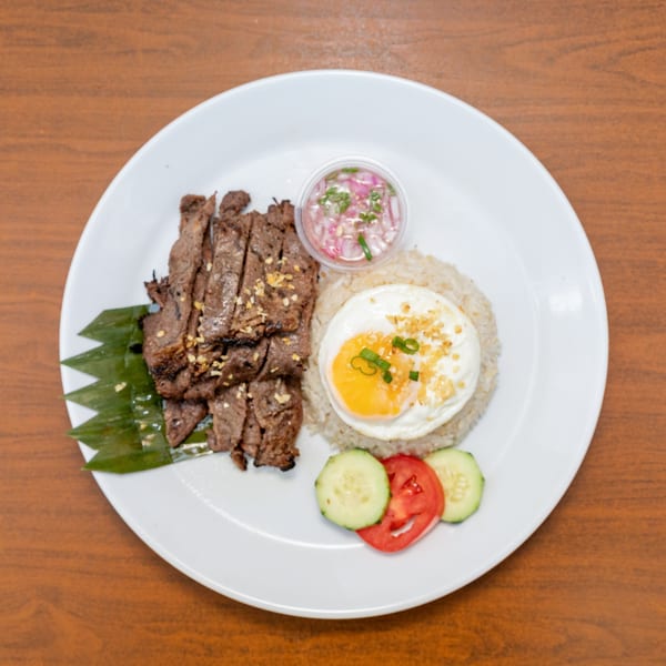 Filipino Tapsilog with sliced beef, fried egg, garlic rice, and a side of pickled onions and vegetables.
